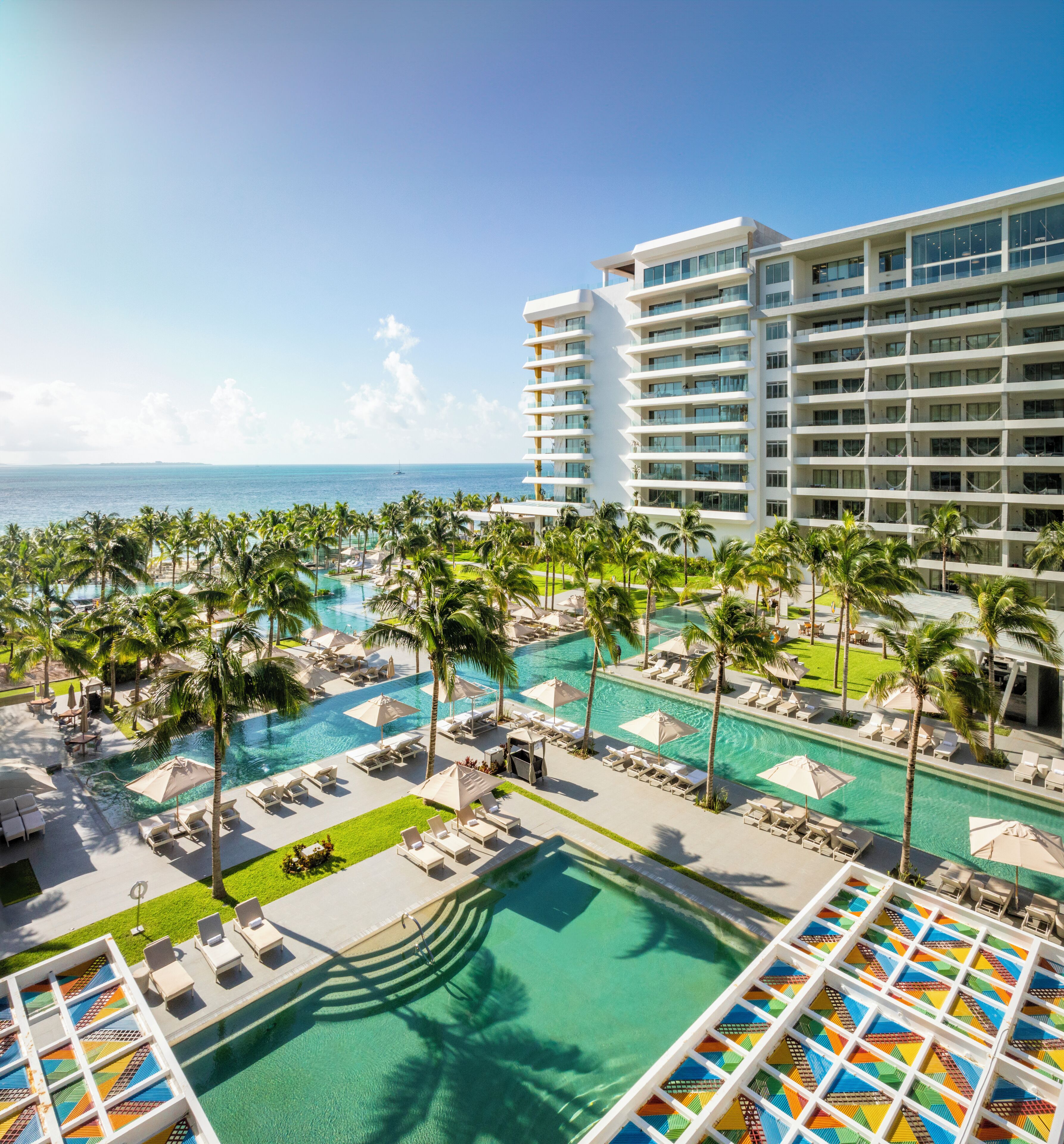A resort with a large pool area, palm trees, and a view of the ocean.