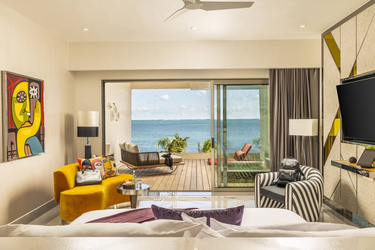 Een hotelkamer met een bed, een bank, een bureau en een televisie. Er is een balkon met uitzicht op de oceaan.