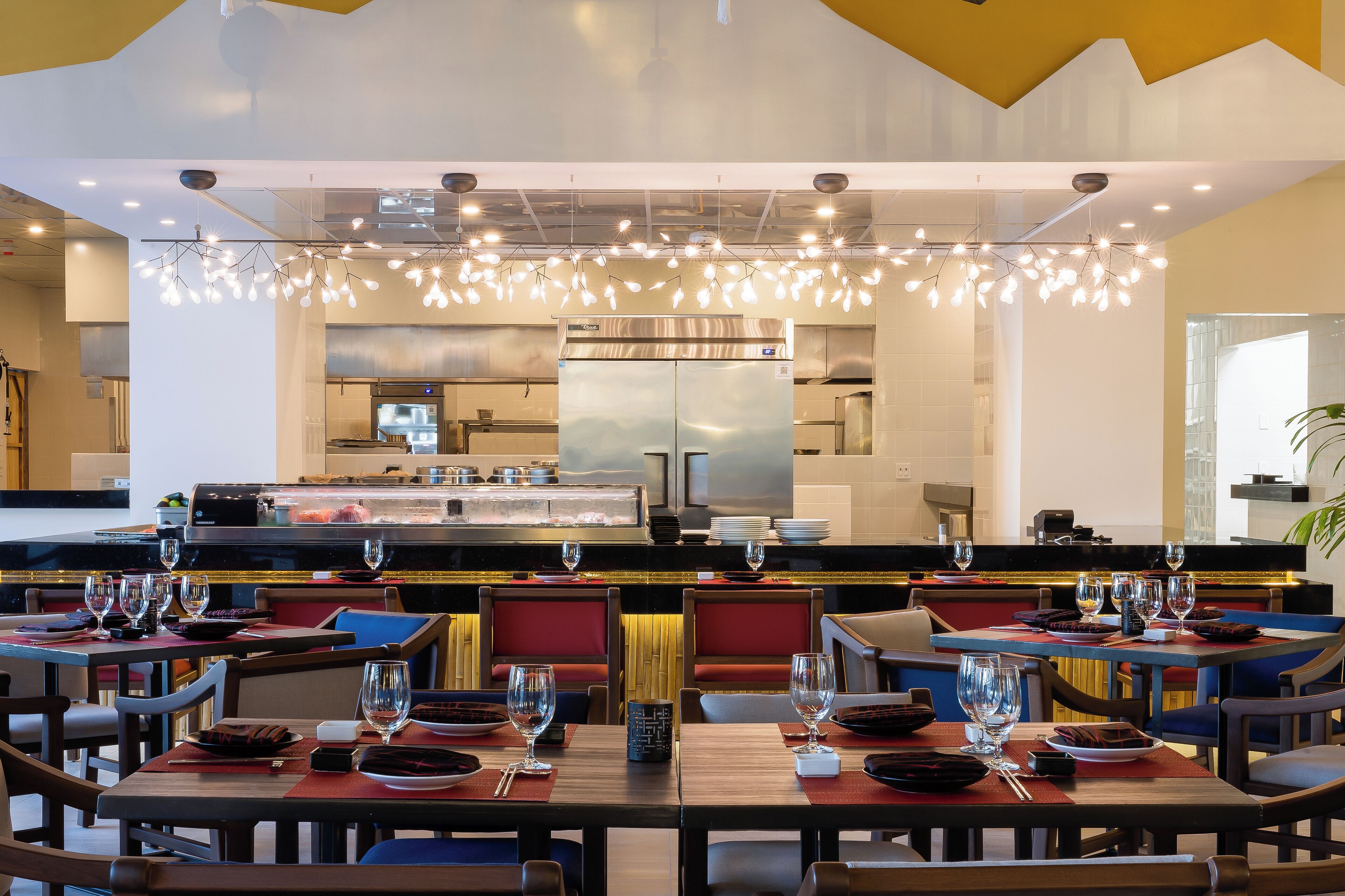 Un restaurante moderno con varias mesas de comedor, cada una con copas de vino y platos, y una zona de cocina al fondo.