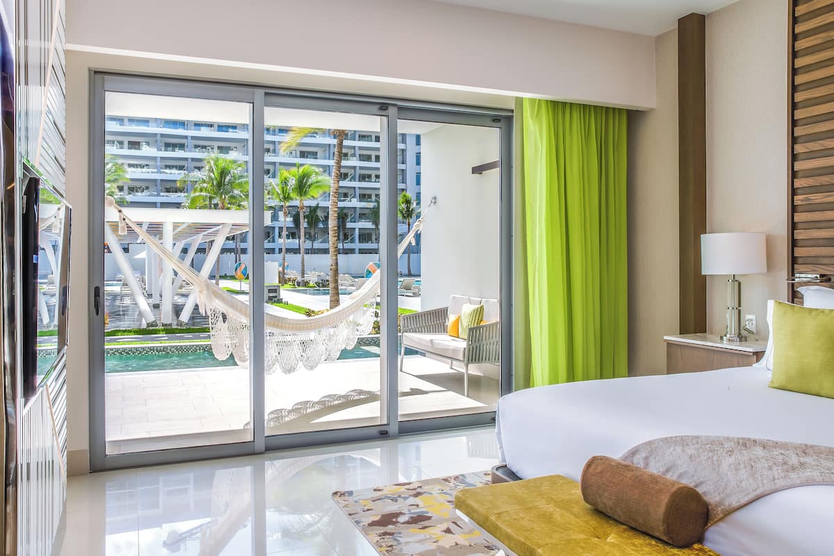Hotelkamer met een groot bed, uitzicht op een zwembad en palmbomen, en een schuifdeur van glas.