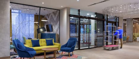 A modern lobby with a yellow sofa, blue armchairs, and a patterned rug.