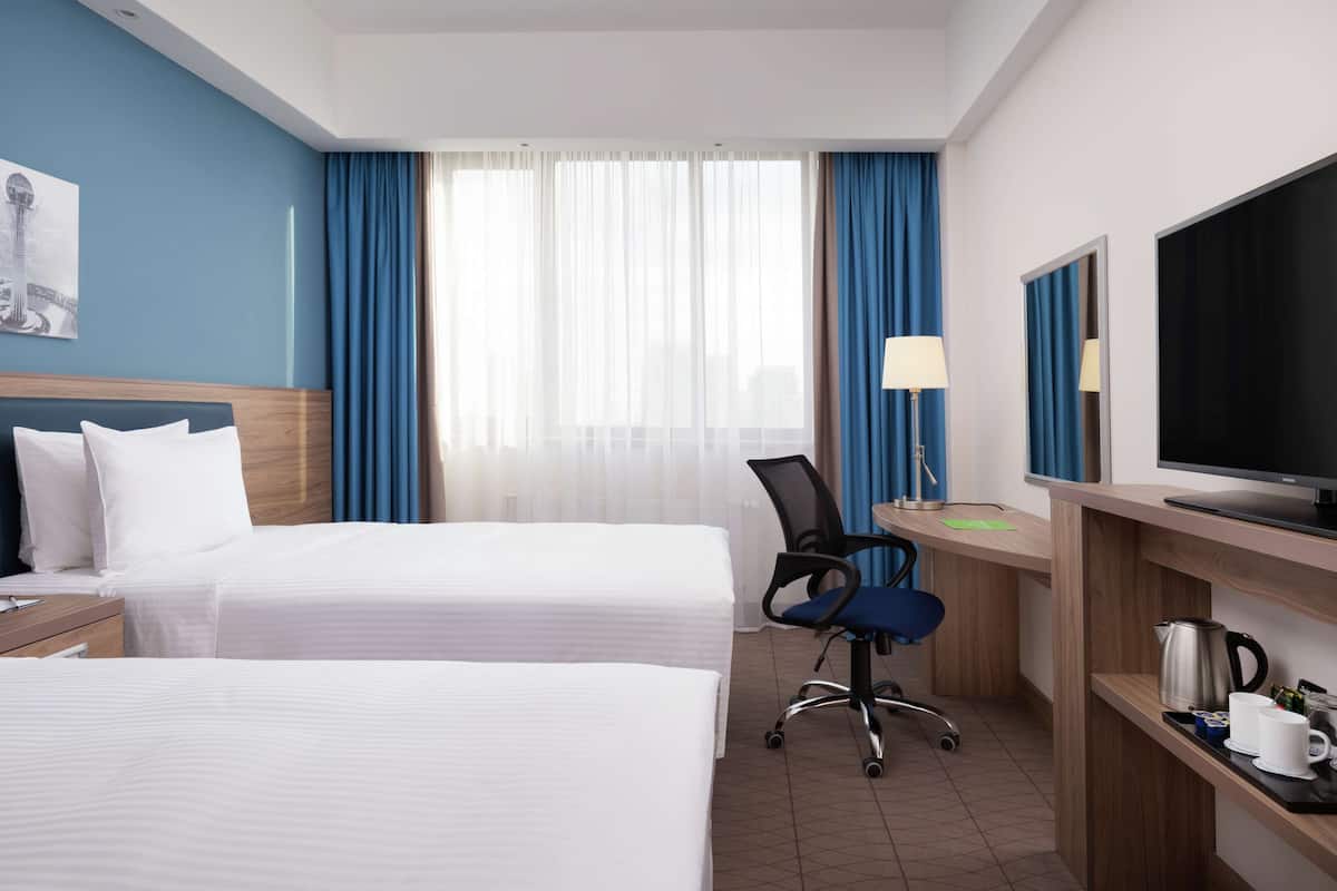 Une chambre d’hôtel avec deux lits, un bureau avec une chaise, une télévision et une machine à café.