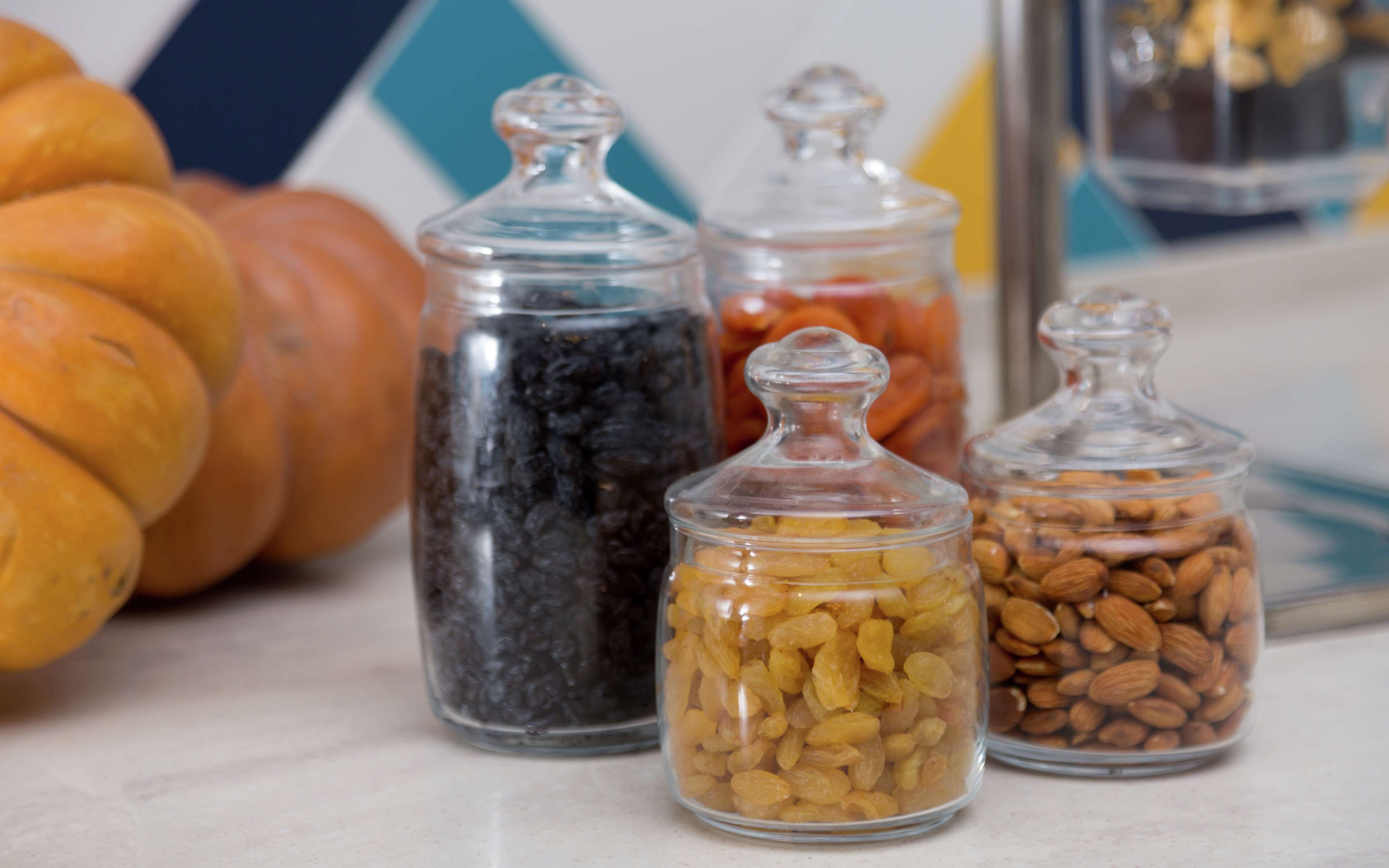 Quatre bocaux en verre contenant différents aliments, avec une miche de pain en arrière-plan.