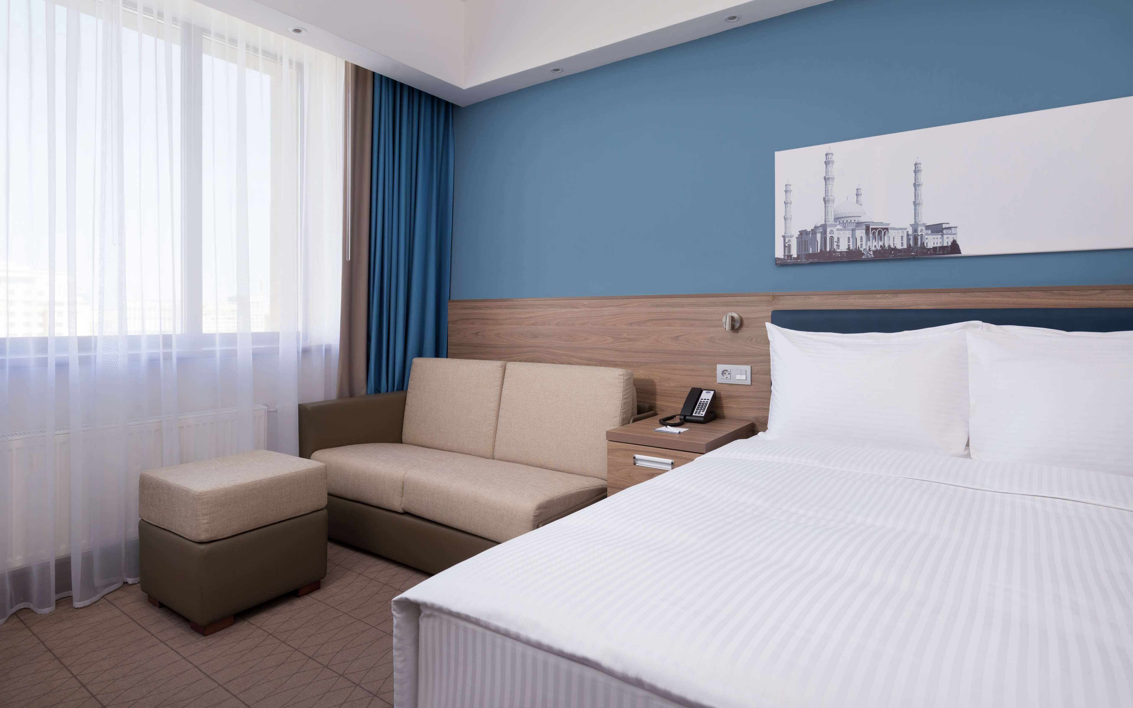 Hotellihuone, jossa on sänky, sohva, rahi, yöpöytä ja puhelin.