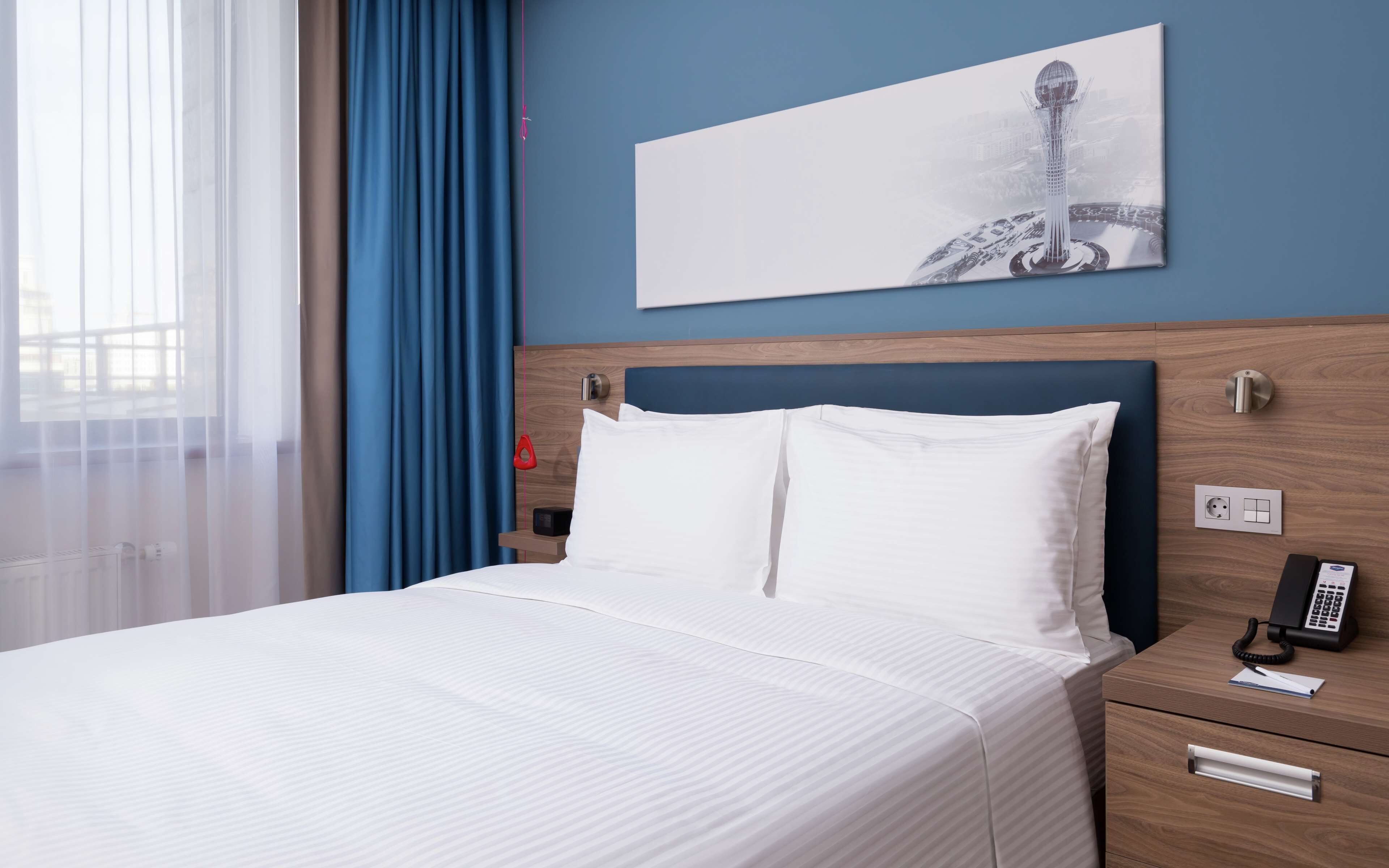 Une chambre d’hôtel avec un lit, une table de chevet avec un téléphone et un tableau au mur.