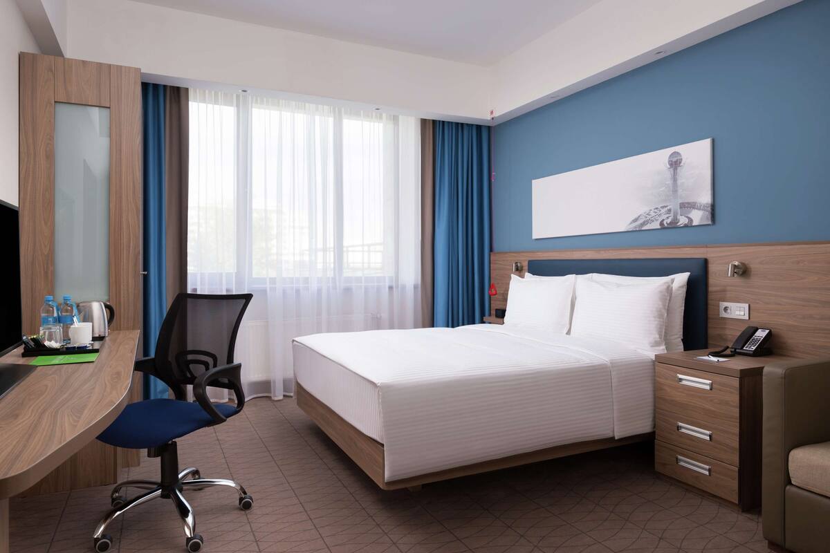 Une chambre d’hôtel avec un lit, un bureau, une chaise, un téléphone et un tableau au mur.