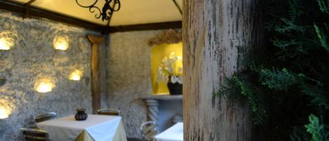 Un restaurante con paredes de piedra, mesas con manteles blancos e iluminación colgante.
