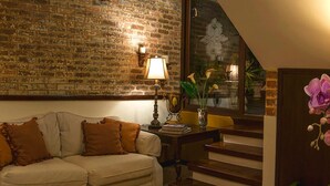 A cozy living room with a brick wall, a sofa with cushions, a lamp, a vase with flowers, and a staircase. - Hostal Villa Toscana (Guatemala City)