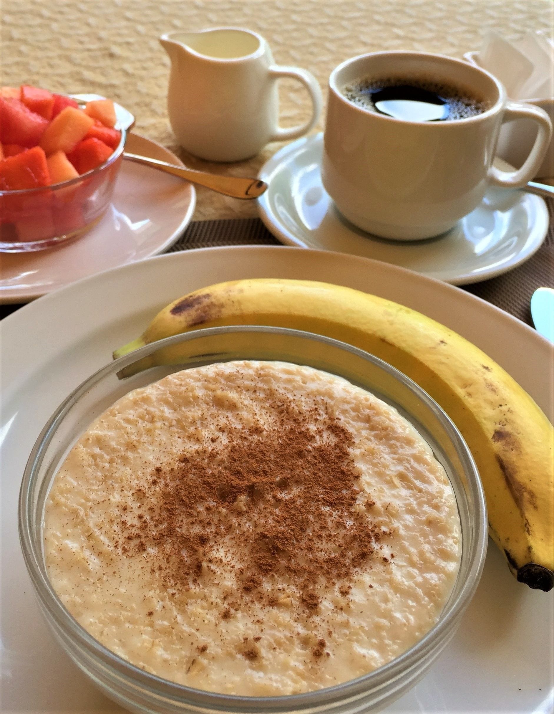 A breakfast setting with a bowl of oatmeal topped with cinnamon, a banana, and a cup of coffee on a table.