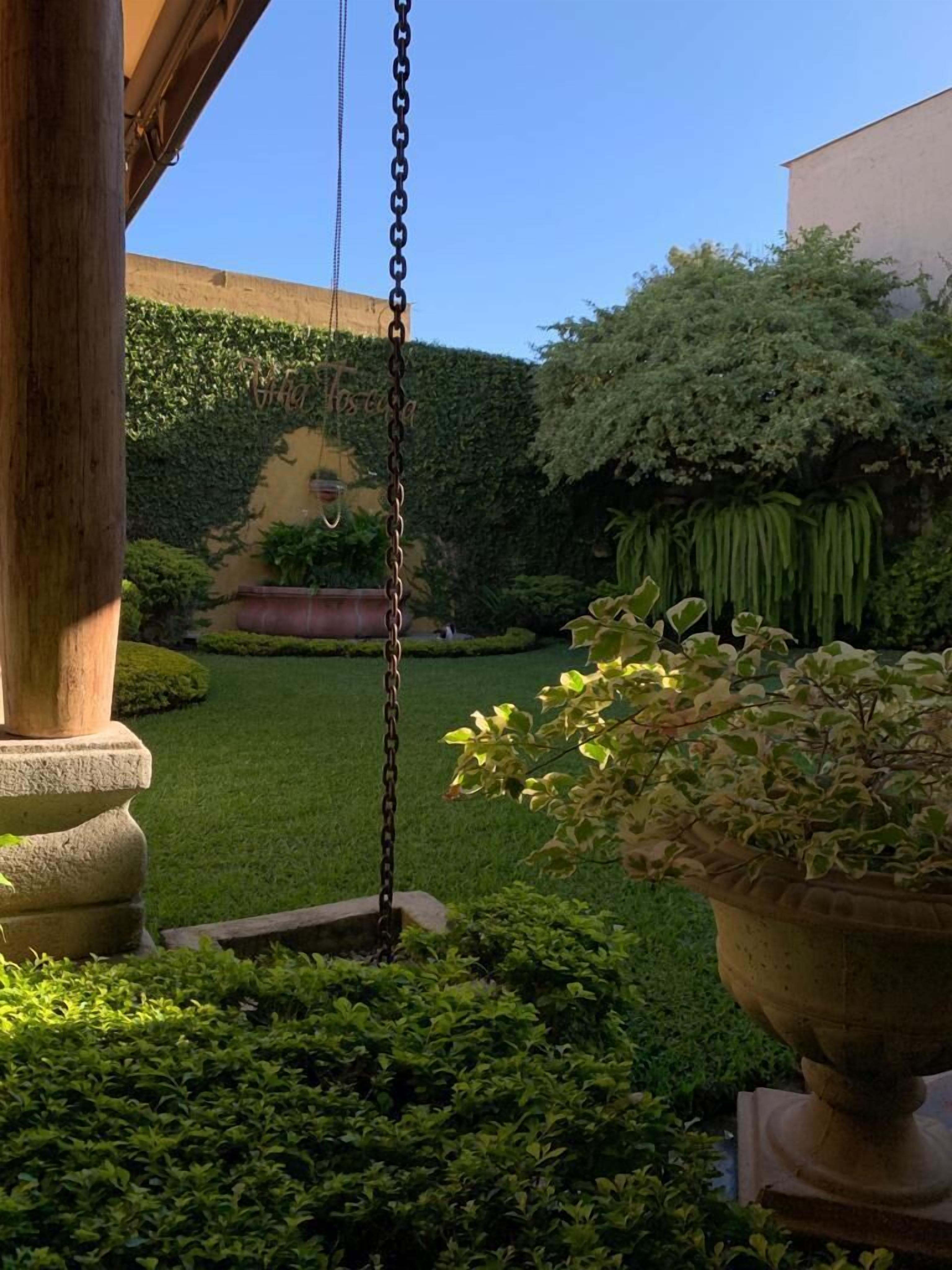 A well-maintained garden with a swing set, neatly trimmed hedges, and a variety of potted plants.