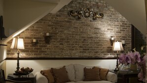 A cozy living room with a brick wall, two lamps, a sofa, and a decorative wall piece. - Hostal Villa Toscana (Guatemala City)