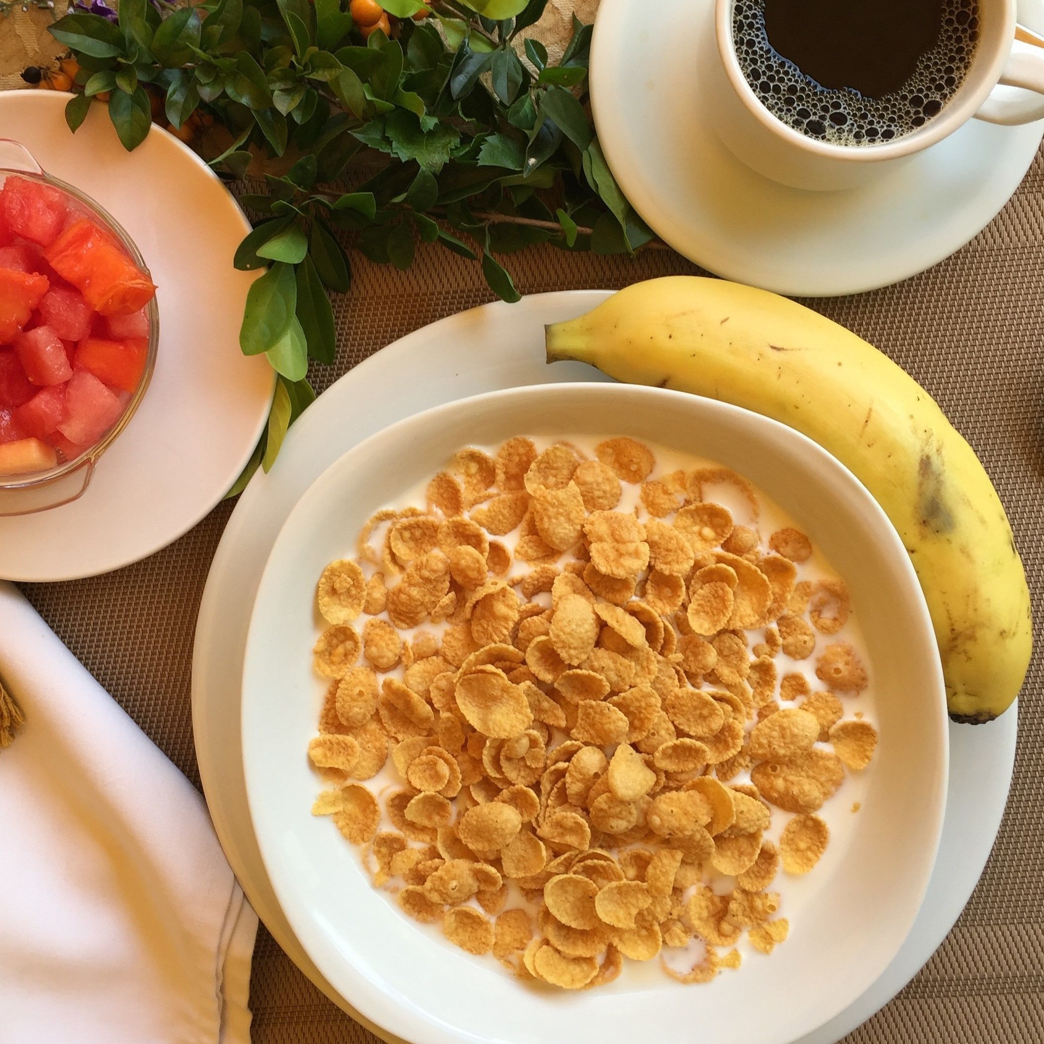 A bowl of cereal with milk, a banana, and a cup of coffee on a table.