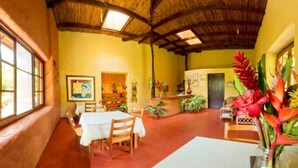 Una habitación con techo de paja, muebles de madera, un mostrador de recepción y plantas tropicales.
