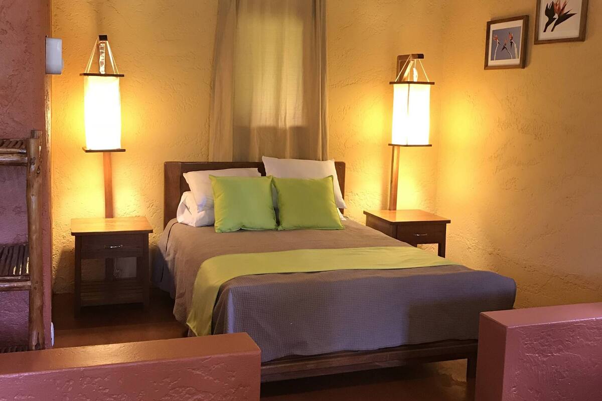 Een slaapkamer met een bed, twee nachtkastjes, een raam met gordijnen en twee wandlampen.