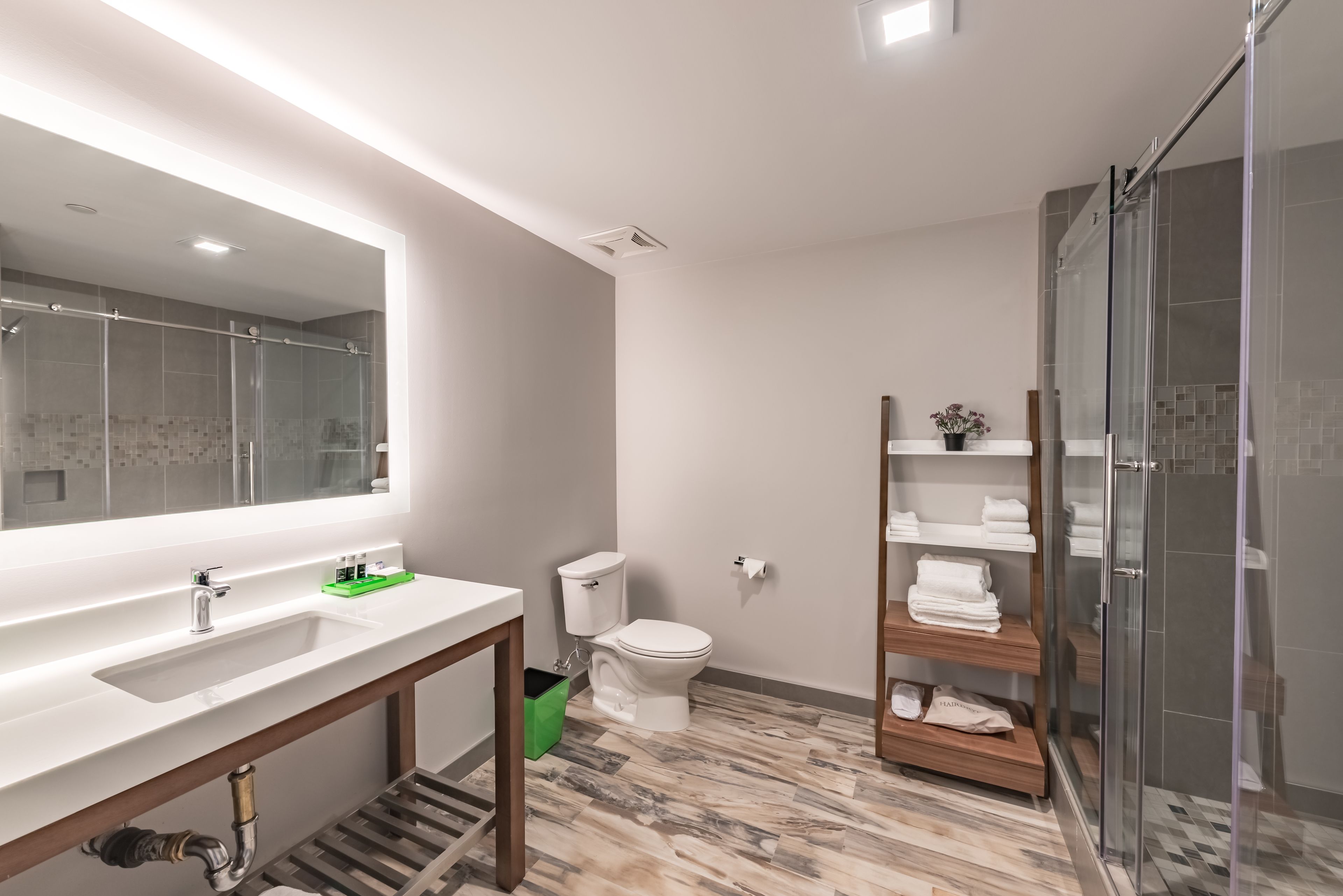 Un baño moderno con un espejo grande, un lavamanos, un inodoro y una zona de ducha.