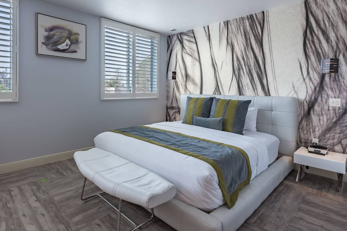 Une chambre moderne avec un grand lit, un banc, une table de chevet et un radiateur fixé au mur.