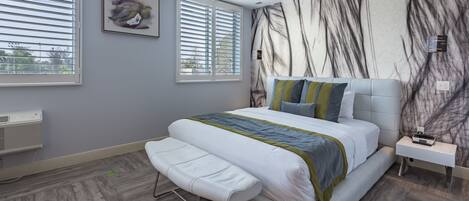 A modern bedroom with a large bed, a bench, a nightstand, and a wall-mounted heater.