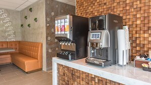 Een moderne koffiehoek met een Nescafé Milano espressomachine en een drankautomaat, een zachte zithoek en een houten achterwand.