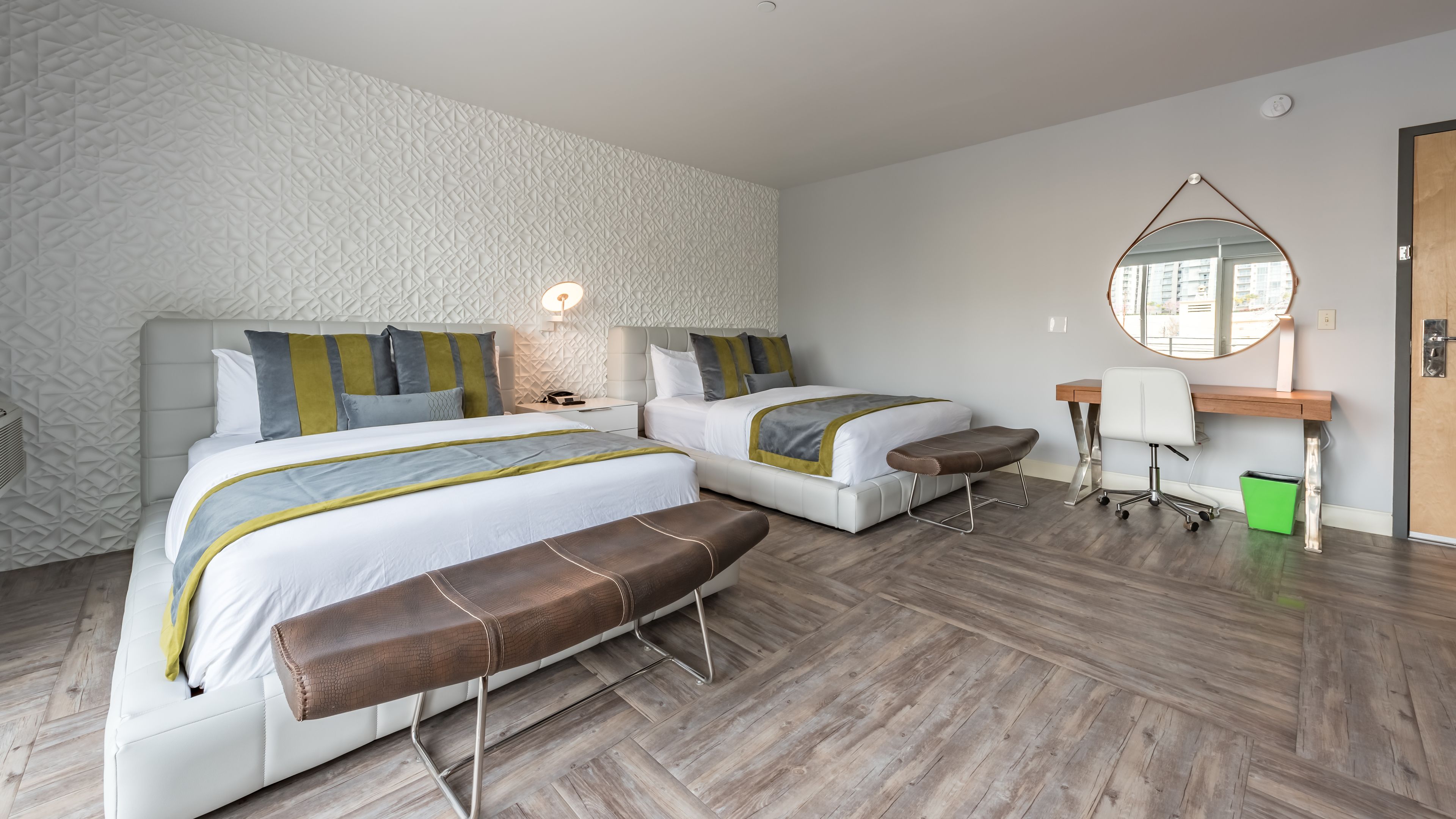 Une chambre moderne avec deux lits, un banc, un bureau et un miroir.