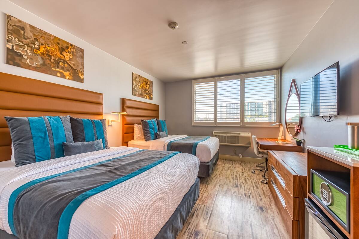 Une chambre d’hôtel avec deux lits, un bureau, une chaise, une télévision et des œuvres d’art accrochées aux murs.
