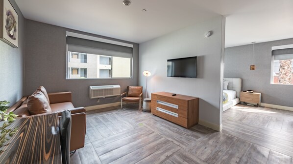 A modern, well-lit living room with a sofa, a chair, a wooden dresser, and a TV mounted on the wall.