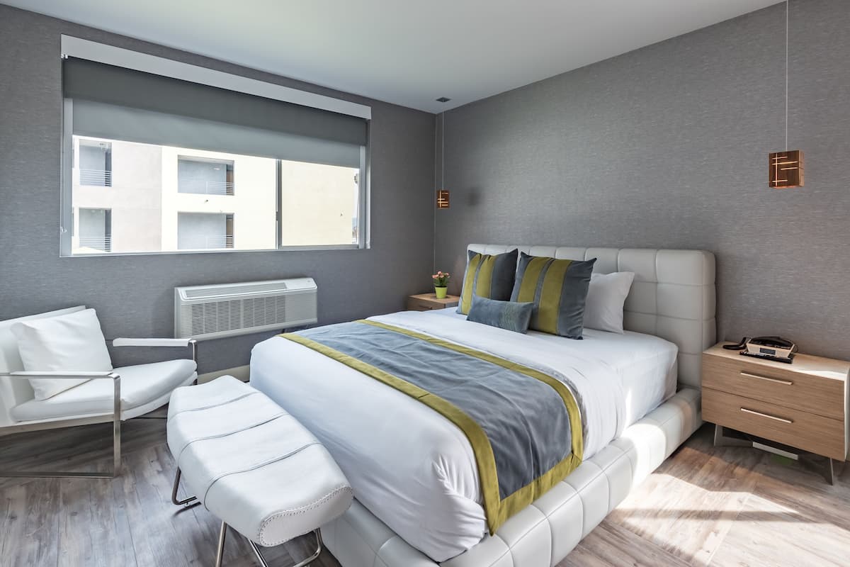Une chambre d’hôtel moderne avec un grand lit, une table de chevet, une chaise et une fenêtre équipée de stores.