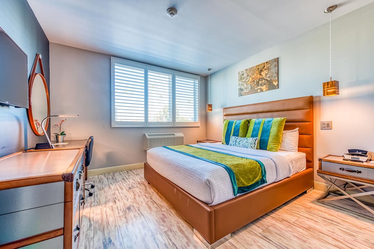 Une chambre moderne avec un grand lit, un bureau, une chaise et une fenêtre avec des stores.