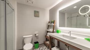 Une salle de bain moderne avec une douche à parois de verre, des toilettes, un lavabo avec un miroir et une poubelle verte.