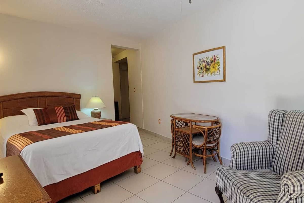 A hotel room with a bed, a chair, a small table, a lamp, and a television.