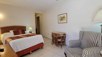 A hotel room with a bed, a chair, a small table, a lamp, and a television.