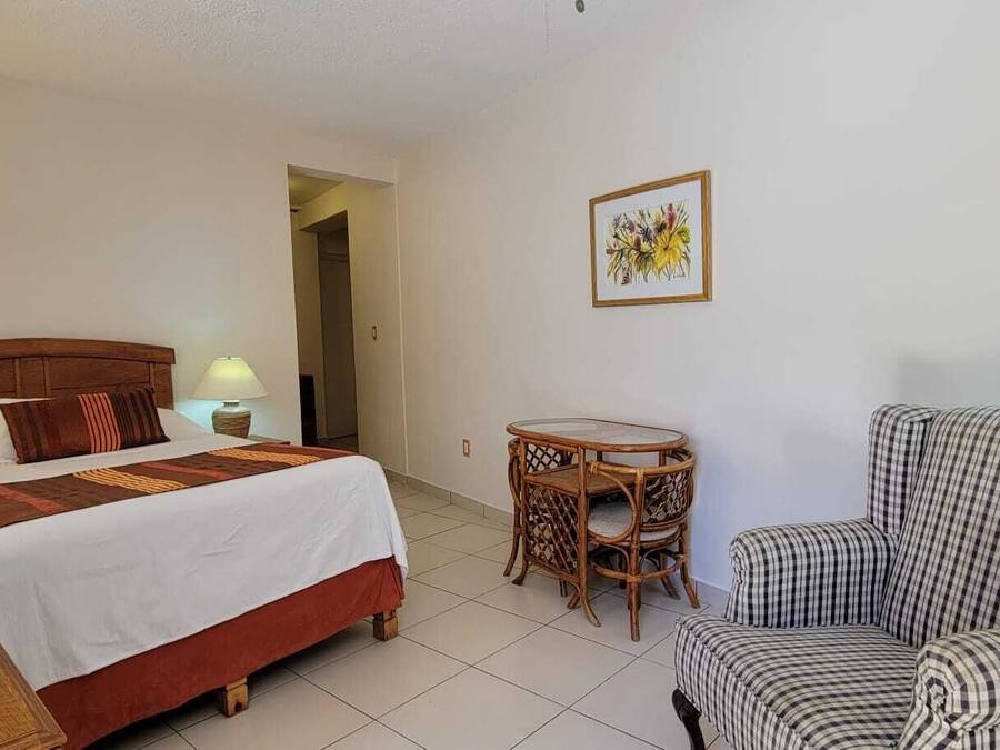 A hotel room with a bed, a chair, a small table, a lamp, and a television.