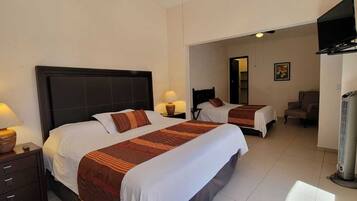 Habitación de hotel con dos camas, televisión, calefacción y una mesita con lámpara.