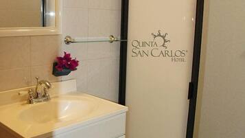 Un baño con lavamanos blanco, espejo y barra para toallas. En la pared hay un letrero que dice "Quinta San Carlos Hotel".