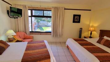 A hotel room with two beds, a TV, a chair, and a window with a view of the outside.
