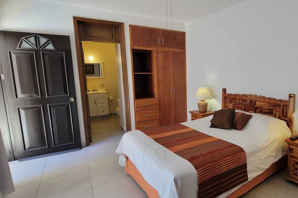 A bedroom with a bed, wooden wardrobe, bedside tables, and a painting on the wall.
