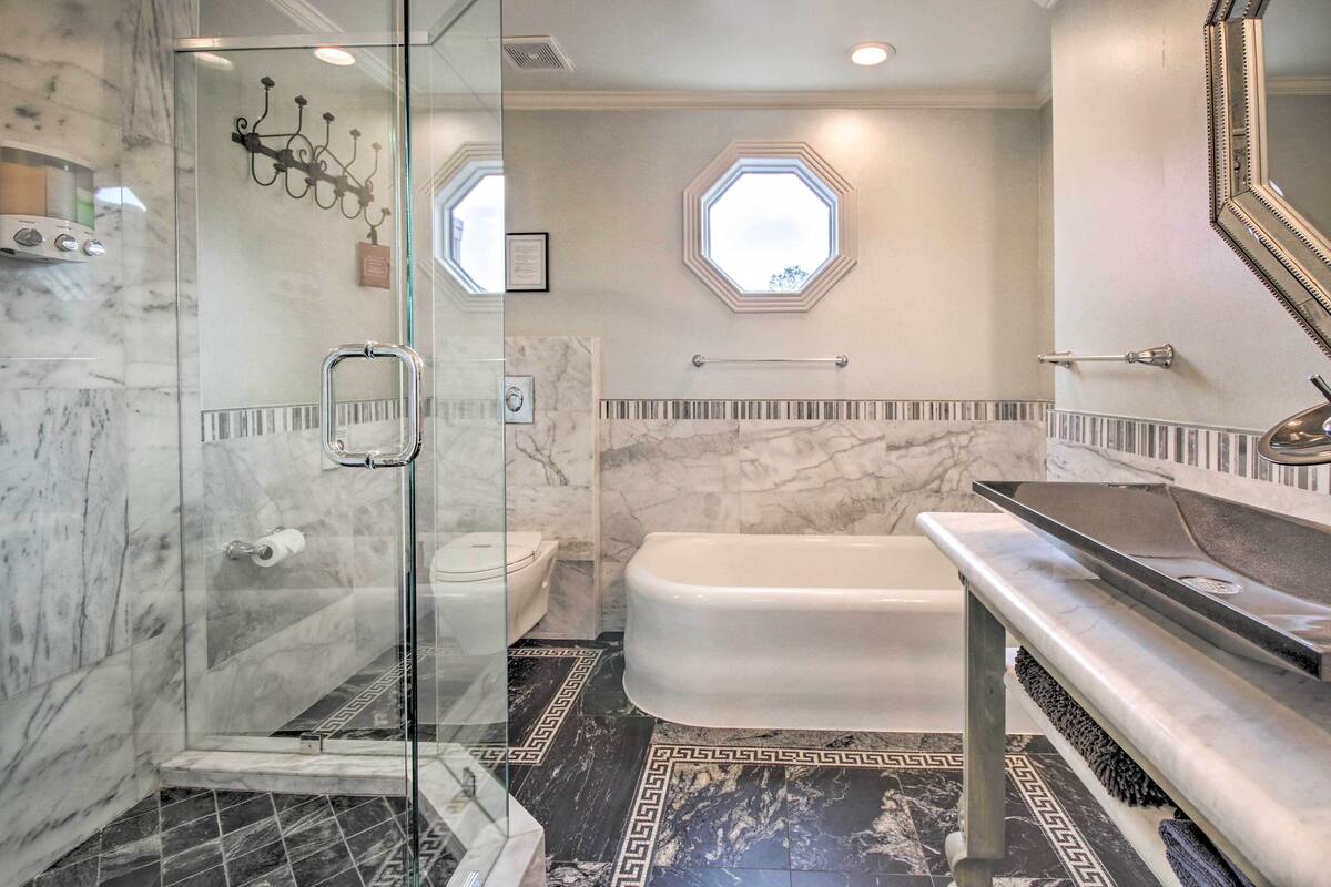 A bathroom with a glass shower enclosure, a bathtub, a vanity with a mirror, and octagonal windows.