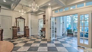 Un pasillo amplio con suelo a cuadros, candelabros elegantes y un espejo grande.