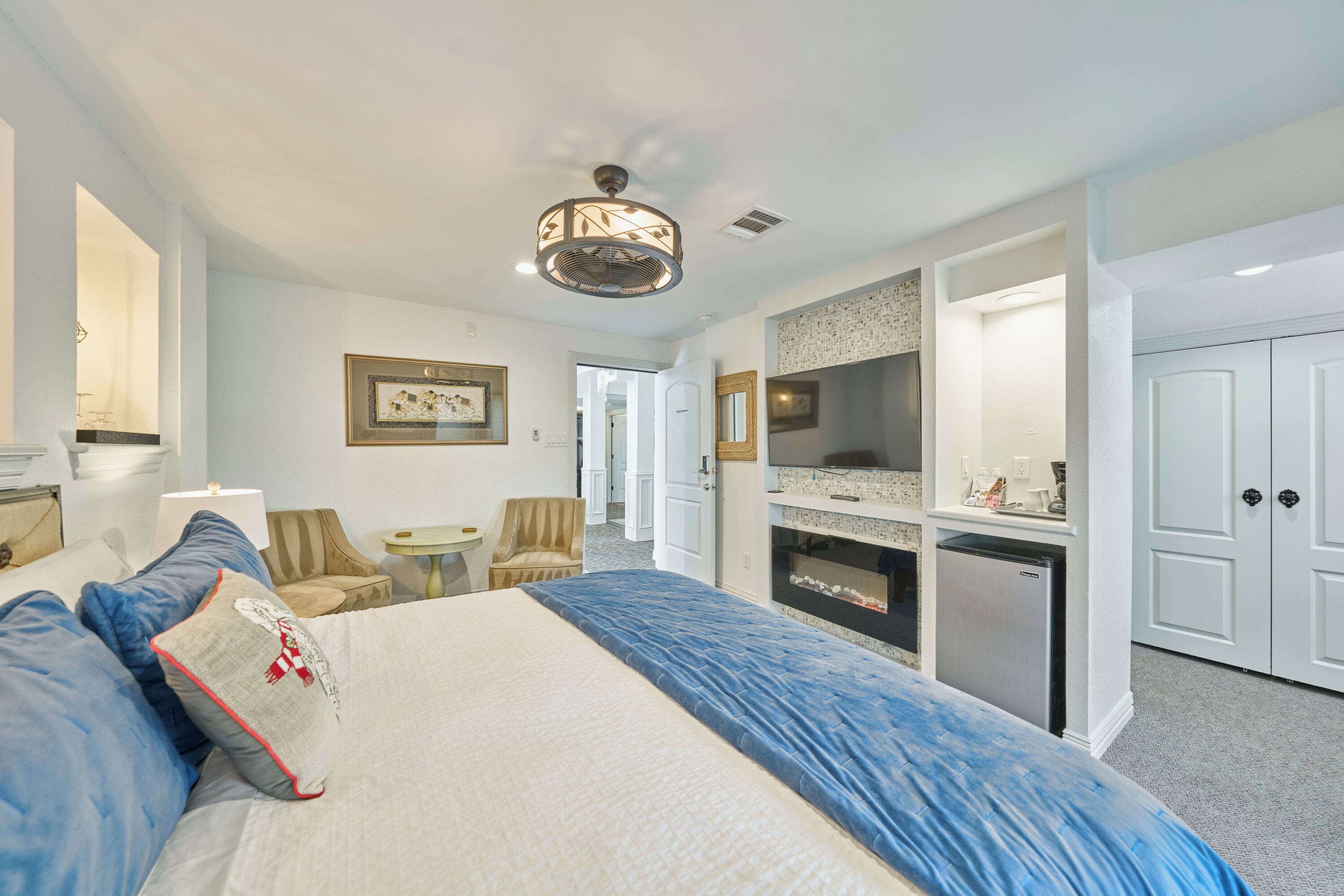 A hotel room with a large bed, a desk, a chair, a television, and a kitchenette.