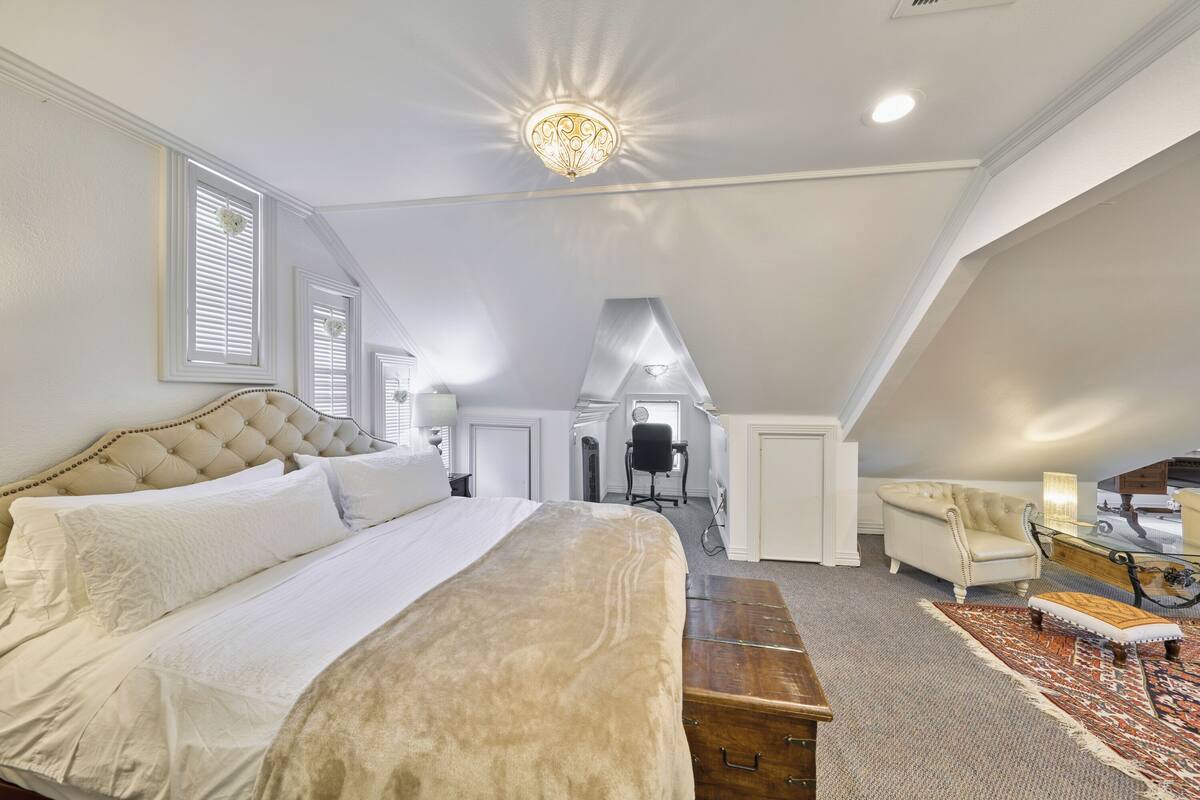 A bedroom with a large bed, a chair, a desk, and a ceiling light.