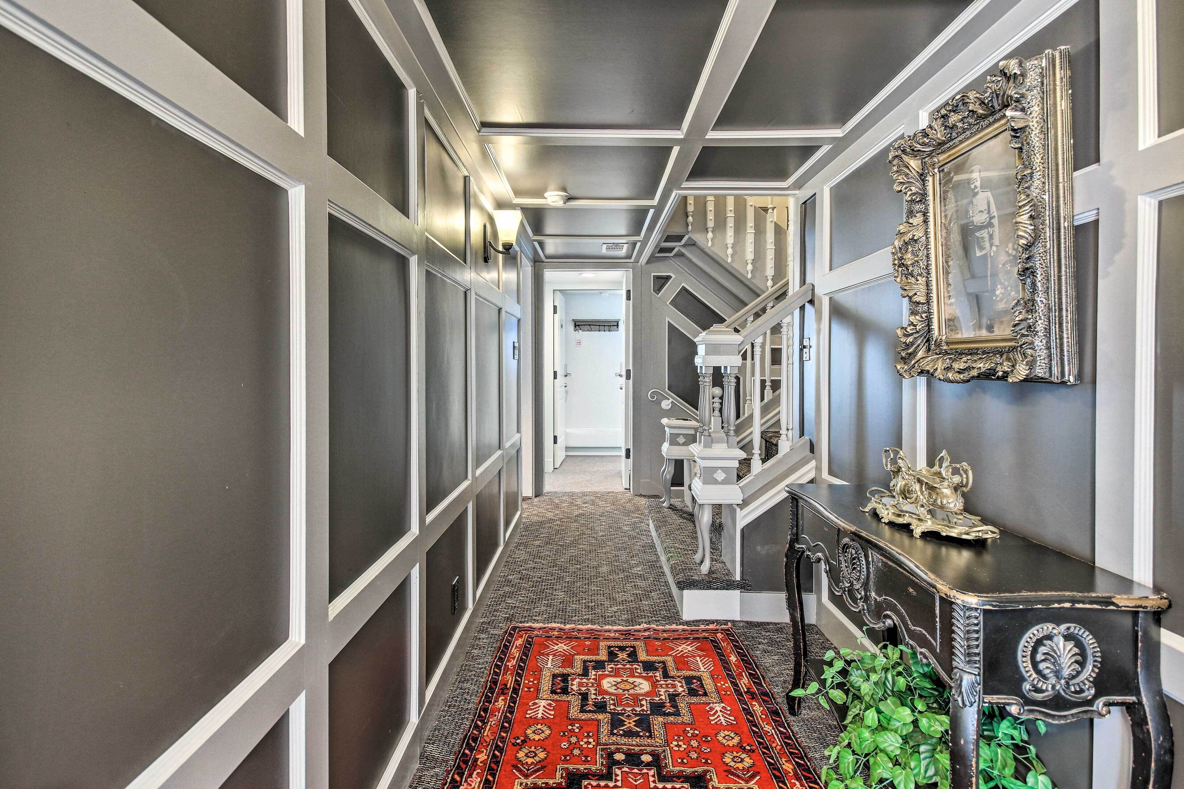 A hallway with a patterned carpet, a staircase, and a decorative console table with a framed picture.