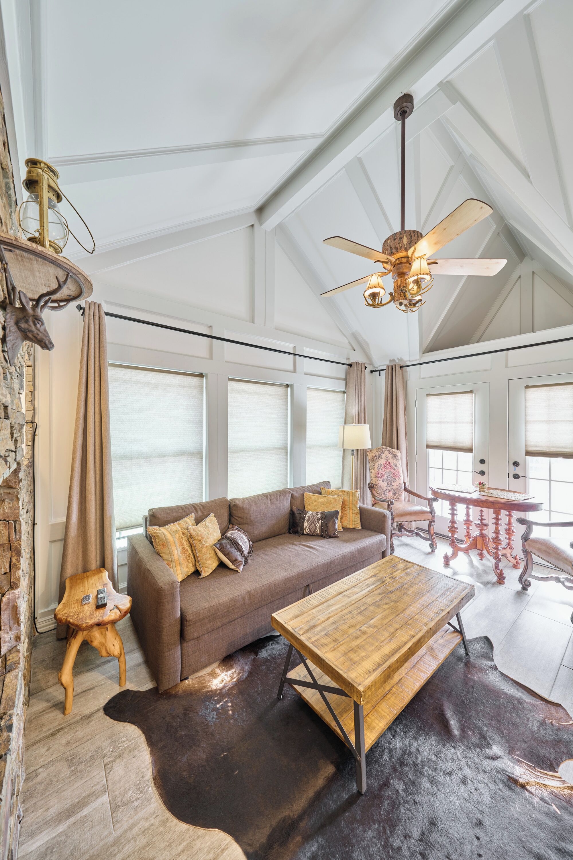 A spacious living room with a high ceiling, a wooden coffee table, a brown sofa, and a ceiling fan.