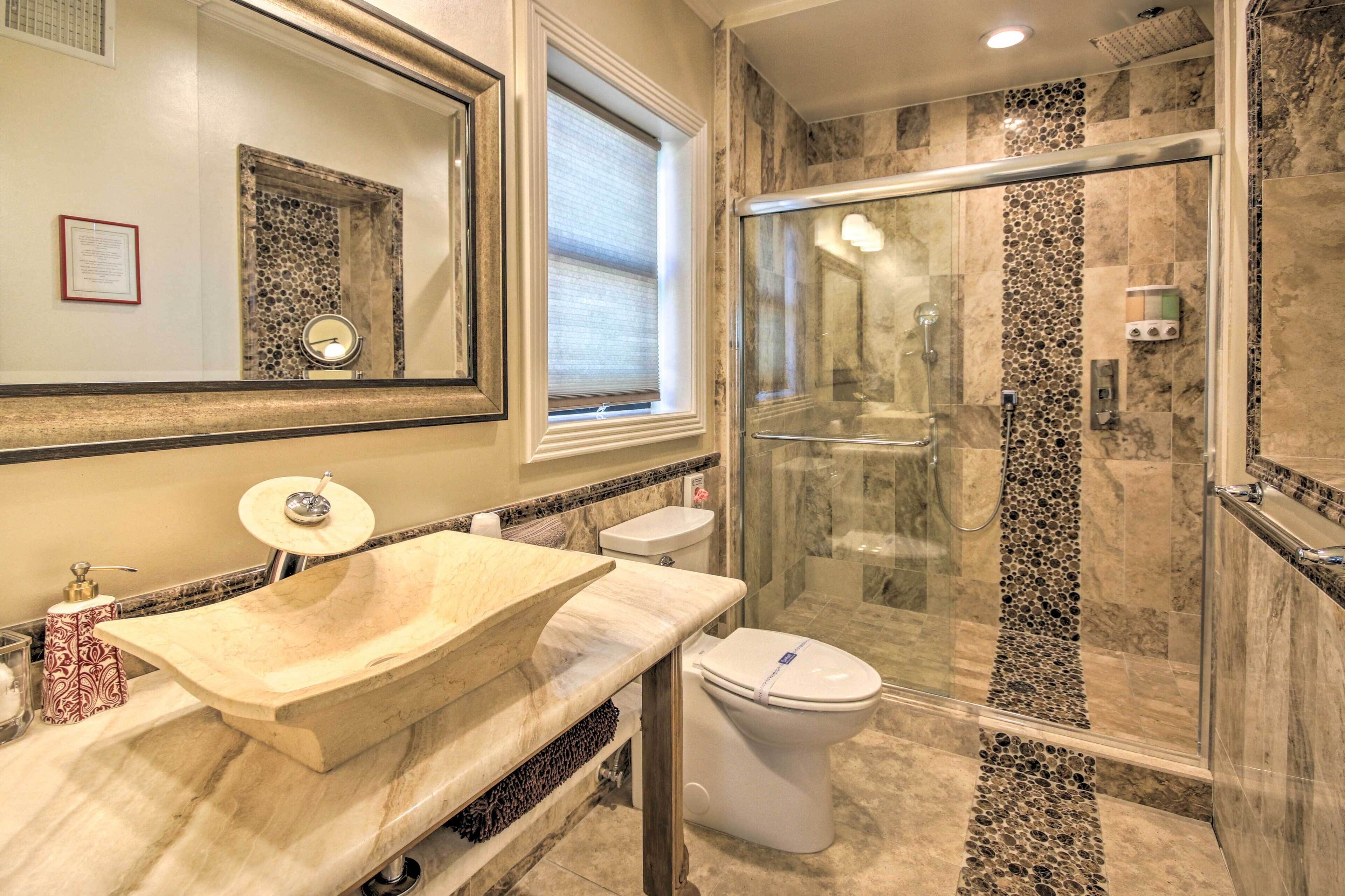 A bathroom with a large mirror, a marble sink, a toilet, and a glass-enclosed shower.