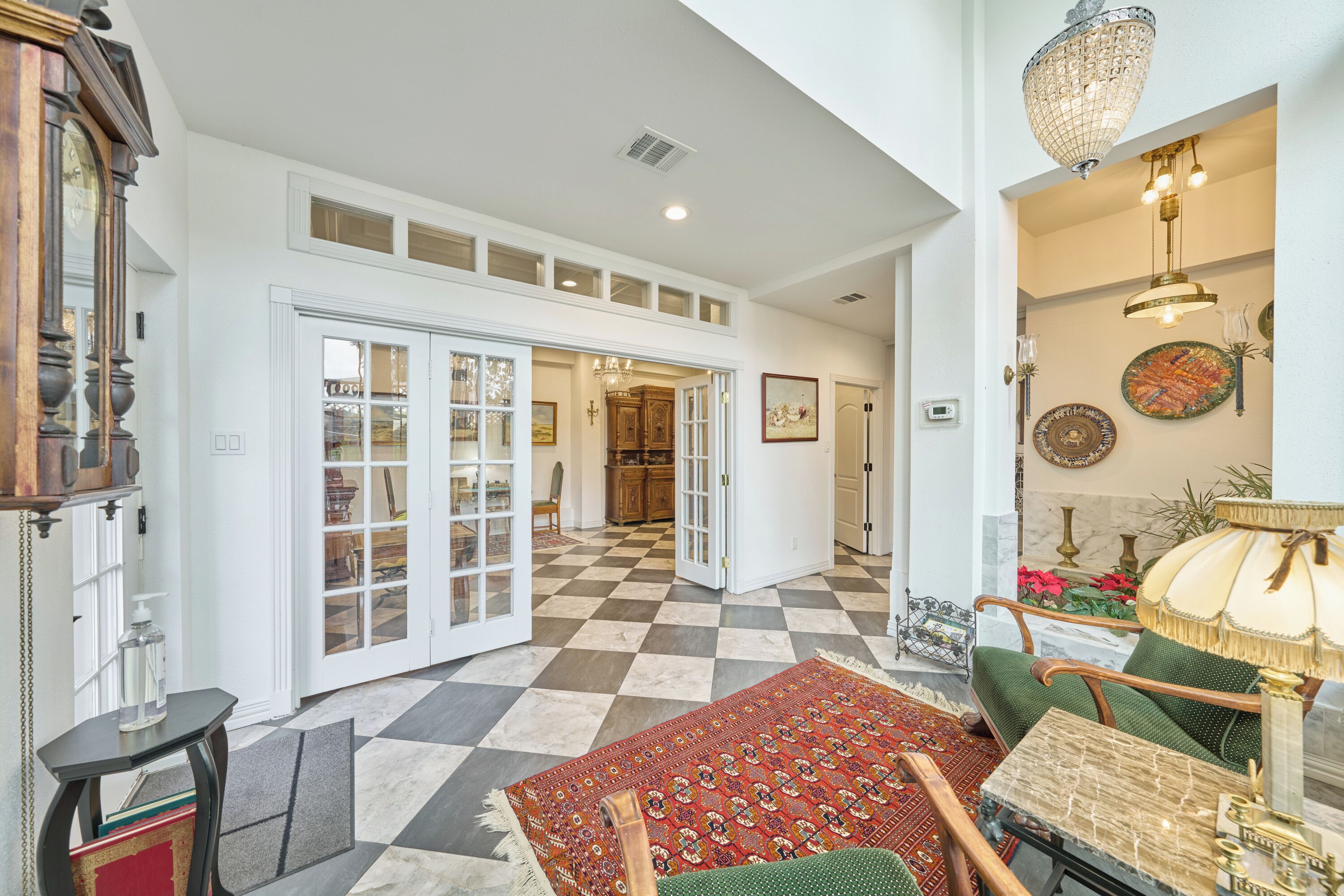 A spacious room with a checkered floor, a green sofa, a wooden table, and a chandelier.