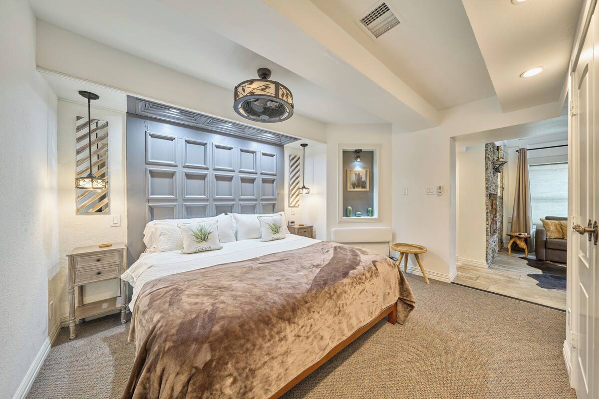 A bedroom with a large bed, a ceiling fan, a window, and a door leading to another room.