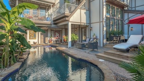 Un área de piscina con un jacuzzi integrado, mobiliario exterior y un balcón con barandilla.