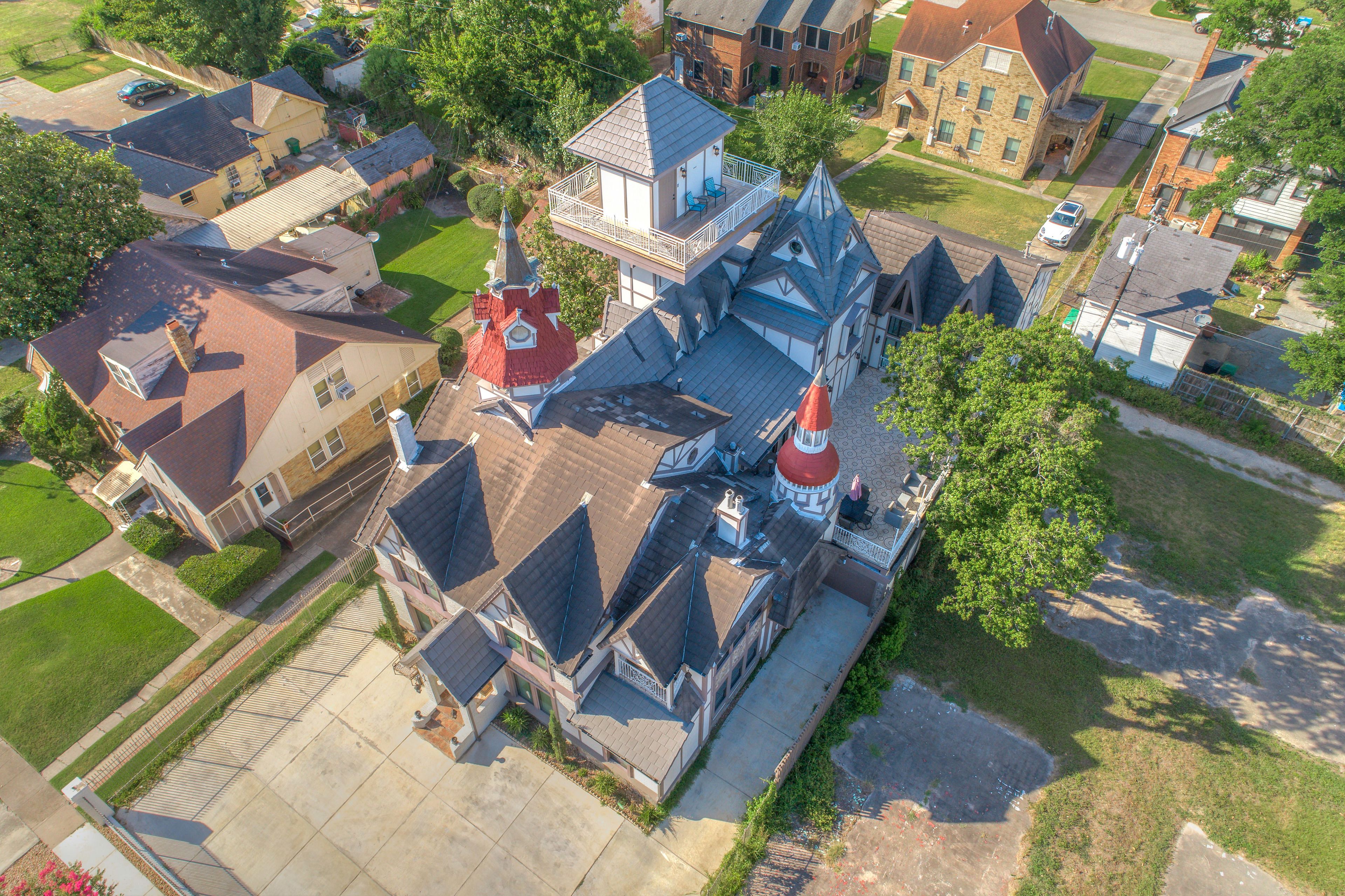 An aerial view of a residential area with a prominent house featuring a large balcony and a turret.