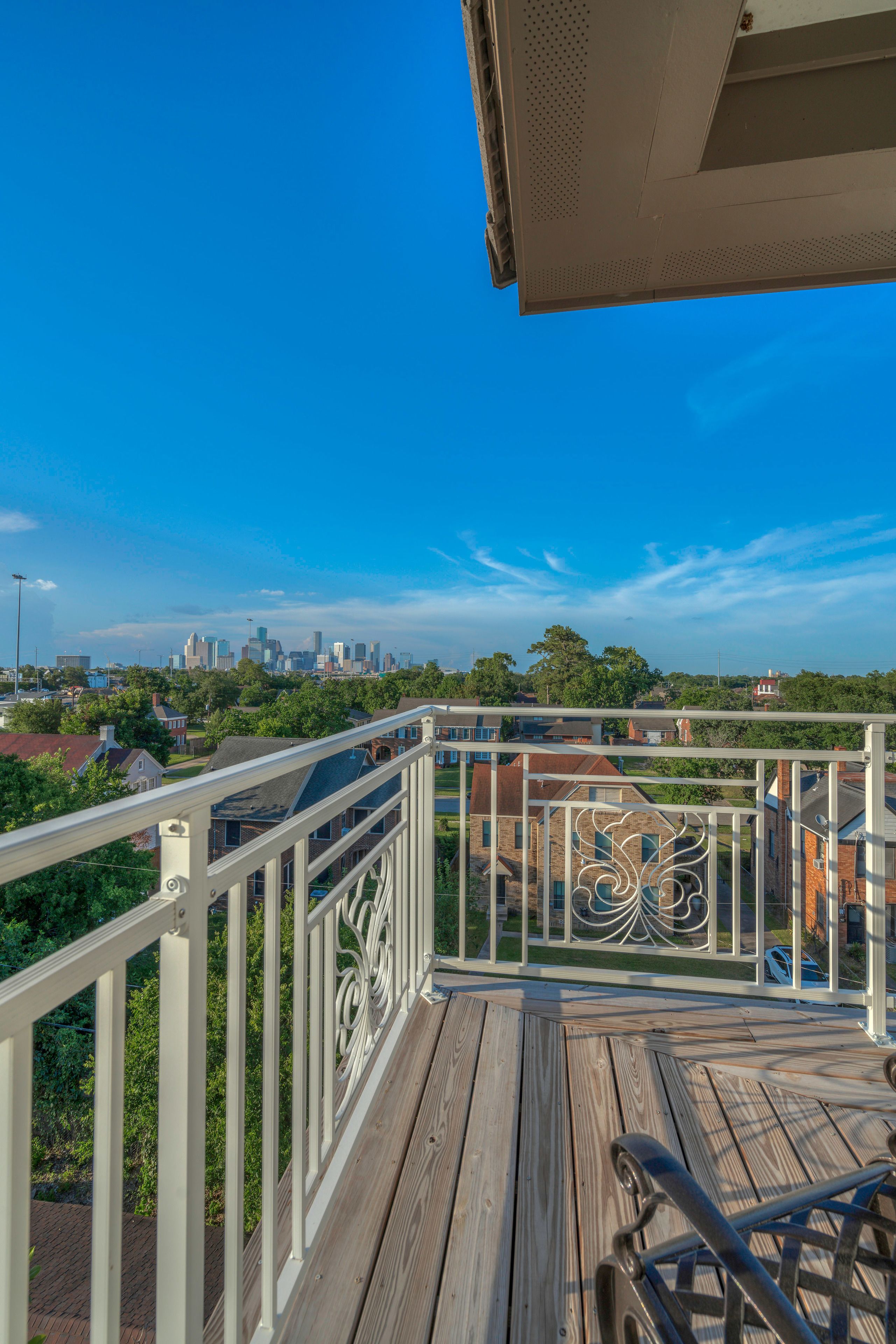 Una terraza de madera con barandilla, con vistas a un horizonte urbano y una zona residencial.