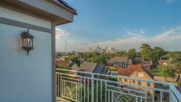 A balcony with a railing, a wall-mounted light fixture, and a view of a residential neighborhood with houses and a distant city skyline.