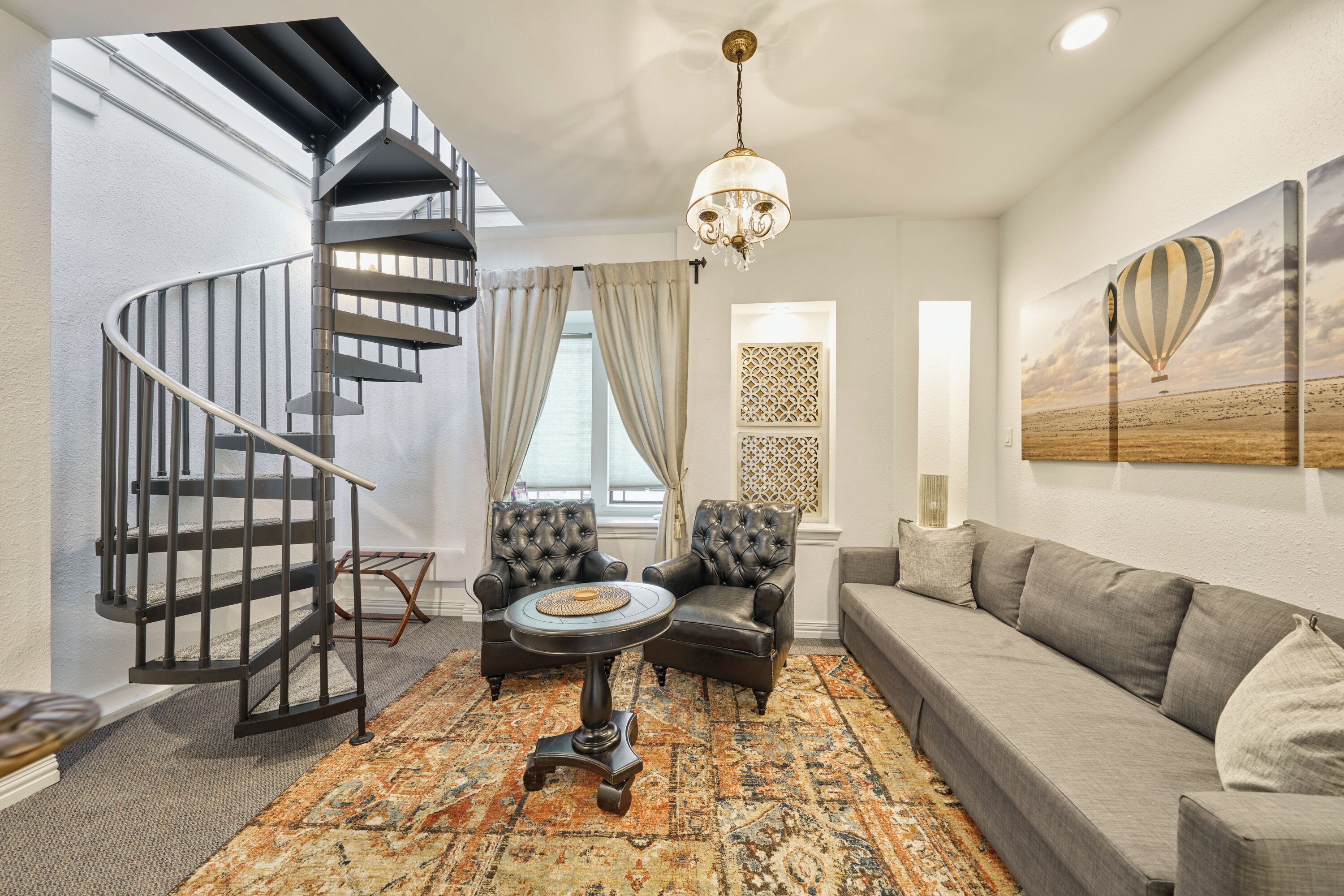 A modern living room with a spiral staircase, leather armchairs, a grey sofa, and a patterned rug.