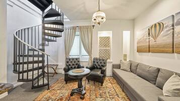 A modern living room with a spiral staircase, leather armchairs, a grey sofa, and a patterned rug.